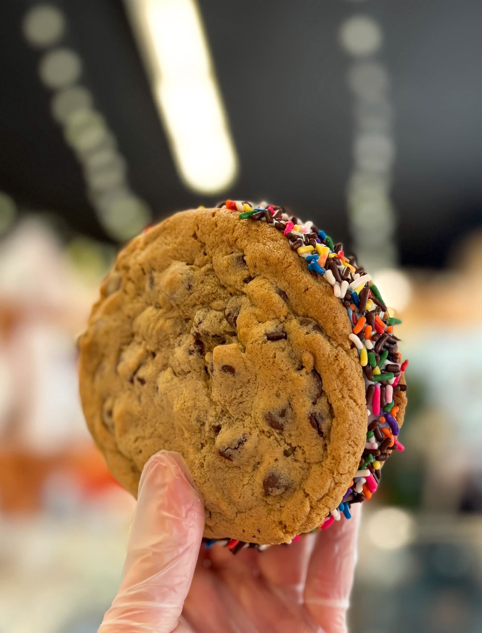 A Sugarmill Sweets chocolate chip cookie sandwich with a colorful sprinkle-covered filling